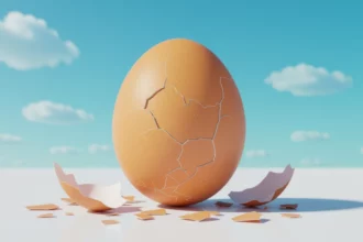 Egy törött tojás, amely körül tojásdarabok hevernek, egy világoskék háttér előtt.
